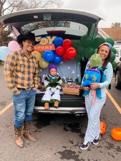 two people standing in front of a car with balloons and decorations on the back door