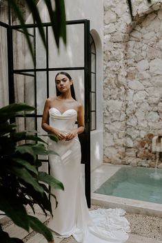 a woman standing in front of a pool wearing a white dress and holding her hands on her hips