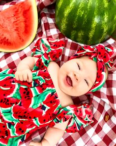 a baby is laying on a red and white checkered blanket next to watermelon