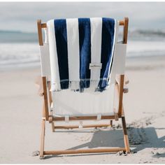 a blue and white striped towel sitting on top of a wooden chair next to the ocean