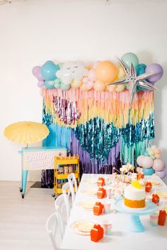 a birthday party with balloons, streamers and cupcakes on a table in front of a rainbow backdrop