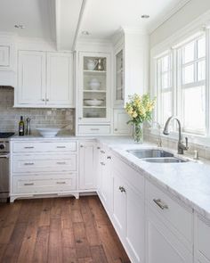 a kitchen with white cabinets and wood flooring is pictured in this image, there are flowers on the window sill