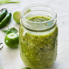 a glass jar filled with green pest next to peppers and other vegetables on a white surface