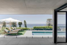 an outdoor swimming pool with lounge chairs and umbrellas on the patio overlooking the ocean