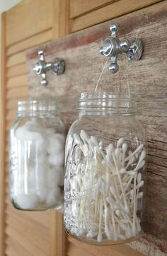 two mason jars filled with white cotton swabs on a wooden wall mounted hook