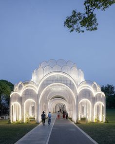 two people walking down a walkway under a lit up archway in the middle of a park