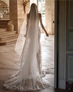 a woman in a wedding dress is walking out the door with her veil over her head