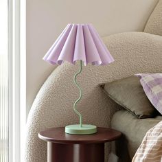 a lamp that is on top of a table next to a bed with pillows and blankets