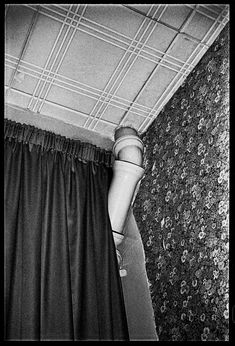 a black and white photo of a curtain in the corner of a room with floral wallpaper