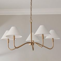 a brass chandelier with five white lamps hanging from it's center point