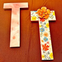 two wooden crosses decorated with flowers on top of a brown cloth covered table, one is painted white and the other has an orange flower in it's center