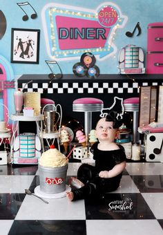 a baby doll sitting on the floor in front of a table with cupcakes