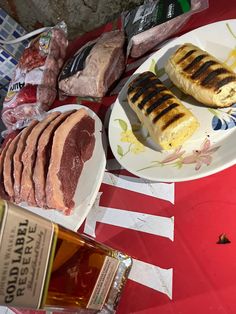 meats, bread and wine on a red table cloth next to an empty bottle