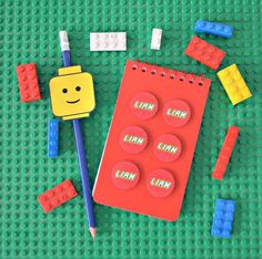 a lego themed notebook and pencils on a green surface with small toys surrounding it