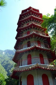 a tall tower with red doors in the middle of trees and mountains behind it on a sunny day