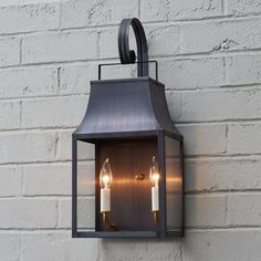 two candles are lit in an old - fashioned lantern light against a white brick wall