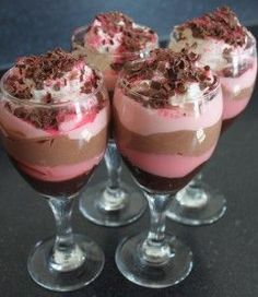 four glasses filled with dessert sitting on top of a black table next to each other