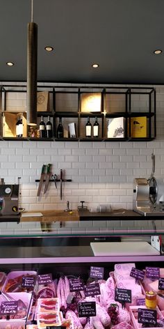 a display case filled with lots of different types of meat in front of a white brick wall