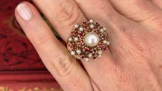 This captivating ring is centered with a post set, cultured saltwater pearl. The top of the ring is four-prong set with sixteen (16) seed pearls and sixteen (16) round single cut garnets. The ring measures 22.5mm at the top, rises 14.2mm above the finger, tapering to 3.7mm wide and 1.4mm thick at the base of the shank. This ring is currently a size 6. Formal White Multi-stone Pearl Ring, Elegant Formal Multi-stone Pearl Ring, Classic Multi-stone Pearl Ring For Formal Occasions, Formal Multi-stone Pearl Ring In Fine Jewelry Style, Elegant Red Pearl Ring For Anniversary, Elegant White Ruby Ring With Multi-stones, Saltwater Pearls, Seed Pearl, Cocktail Ring