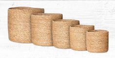 six natural jute wastebaskets lined up against a white wooden wall