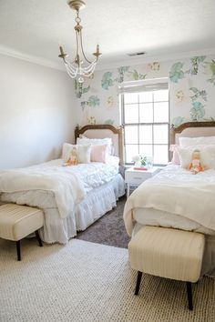 two twin beds in a bedroom with floral wallpaper and chandelier above them