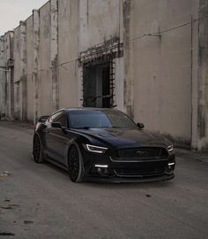 a black sports car parked in front of an old building with graffiti on the walls