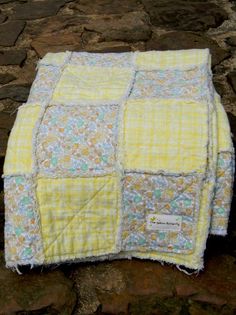 a yellow and blue patchwork baby blanket on the ground with rocks in the background