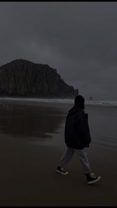 a person walking on the beach in front of an island with a rock outcropping