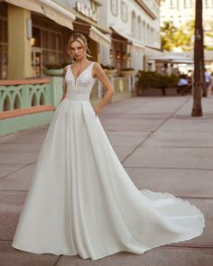 a woman in a white wedding dress standing on the sidewalk with her hands on her hips