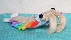 a stuffed dog laying on top of a bed with a rainbow colored toy in it's mouth