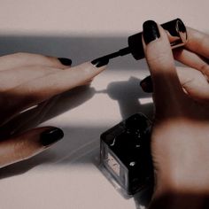 two hands with black manicures on their nails and one hand holding a nail brush