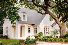 a white house with trees and bushes around the front door is surrounded by greenery