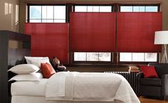 a large bed sitting in a bedroom next to two windows with red shades on them