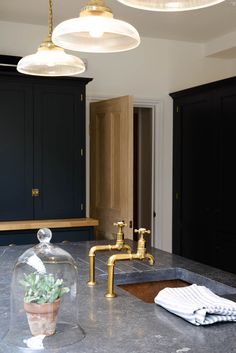 a kitchen with marble counter tops and gold faucet lights above the sink in front of black cabinets