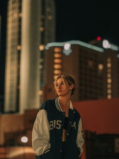 a woman standing in front of a city skyline at night with her hands on her hips