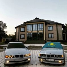 two white bmws parked in front of a large building with windows on each side