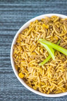 a white bowl filled with yellow rice and green onions on top of a blue table cloth