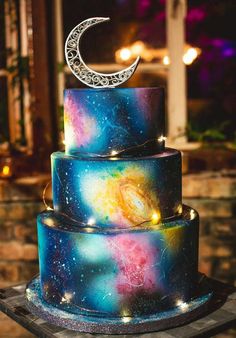 a multi - tiered cake with the moon on top is decorated with galaxy and stars