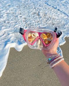 a person wearing goggles and holding up some shells in front of the ocean water