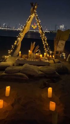 candles are lit in front of a teepee tent on the beach at night with city lights