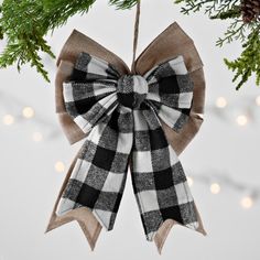 a christmas ornament hanging from a tree with lights in the background and plaid bow on it