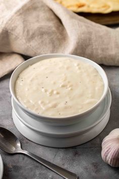 a white bowl filled with cream sauce next to two plates and spoons on a table