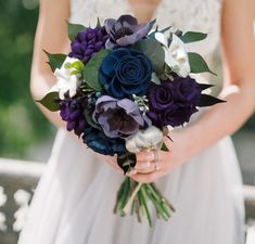 a woman holding a bouquet of flowers in her hands and wearing a wedding dress with white, purple, and blue colors