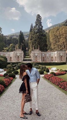 a man and woman kissing in front of a garden