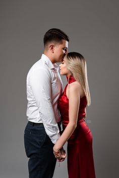 a man and woman in red dress standing next to each other with their arms around each other