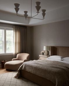 a bedroom with a large bed and two chairs in front of a window that has curtains on the windowsill