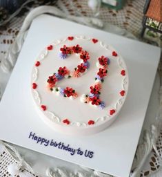 a white cake with red and blue flowers on it that says happy birthday to us