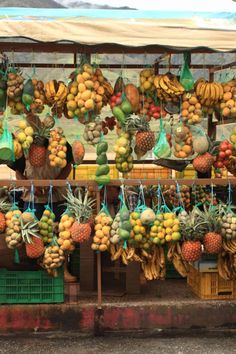 an outdoor fruit stand with bananas, pineapples and other fruits hanging from it