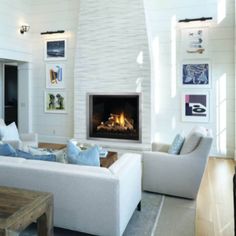 a living room filled with white furniture and a fire place in the middle of it