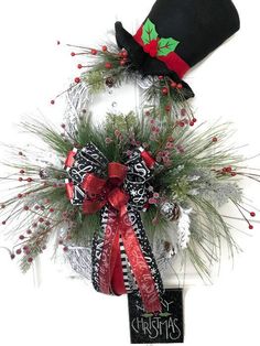 a christmas wreath on top of a white wall with a black hat and red ribbon